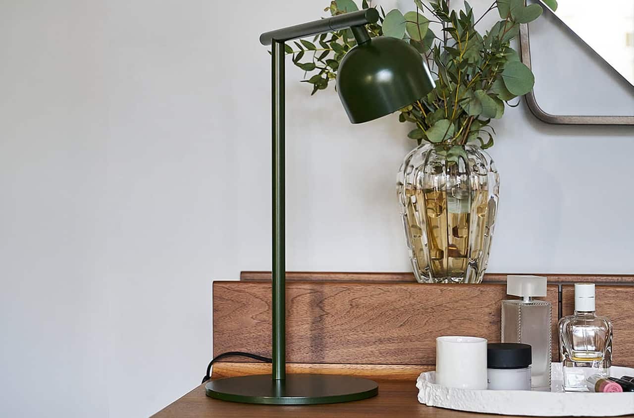 Moderne Tischleuchte in Grün mit schlichtem Design auf einer Kommode.